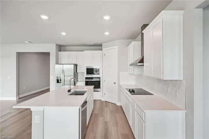 Kitchen featuring stainless steel appliances, a sink, light wood finished floors, backsplash, and an island with sink