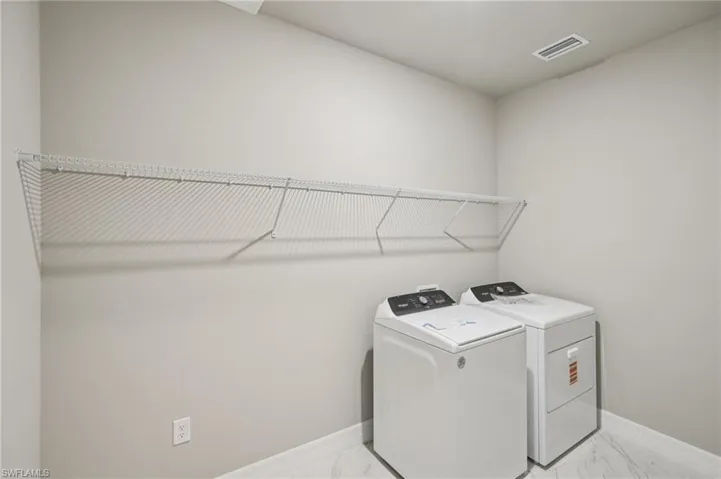 Laundry room featuring light marble finish floors, washer and dryer, and baseboards