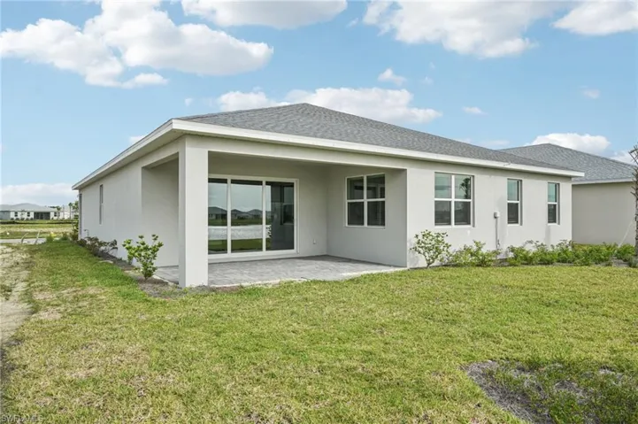 Back of house with a patio area, a lawn, stucco siding, and a shingled roof