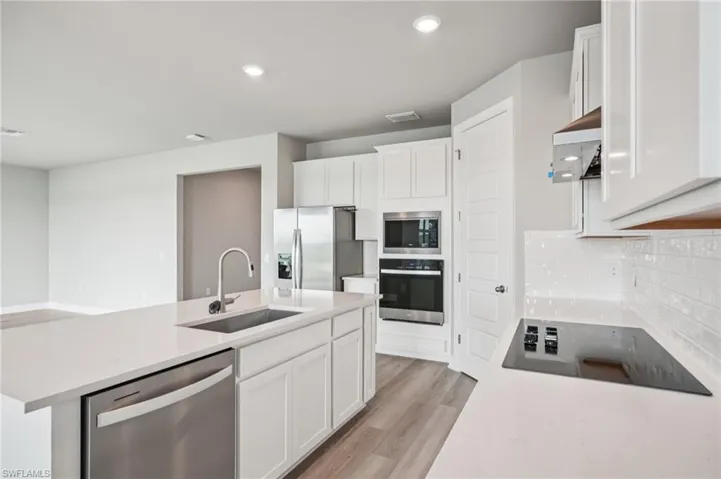 Kitchen featuring stainless steel appliances, a sink, white cabinets, light countertops, and recessed lighting