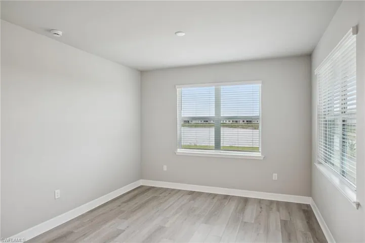 Empty room with light wood-style floors, baseboards, and a smoke detector