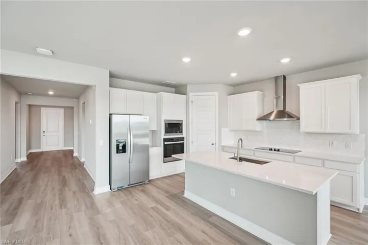 Kitchen featuring appliances with stainless steel finishes, wall chimney exhaust hood, a sink, decorative backsplash, and light wood-style flooring