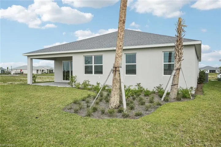 Back of property with stucco siding, a shingled roof, a lawn, and a patio area