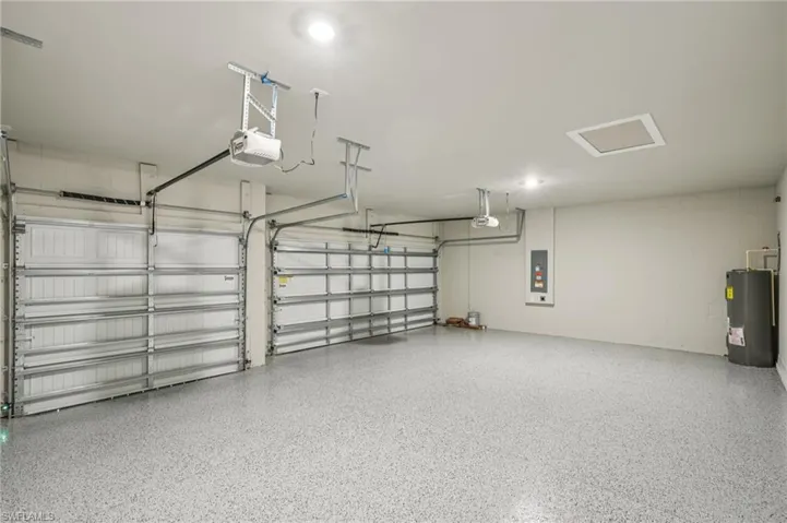 Garage with a garage door opener, electric water heater, electric panel, and concrete block wall