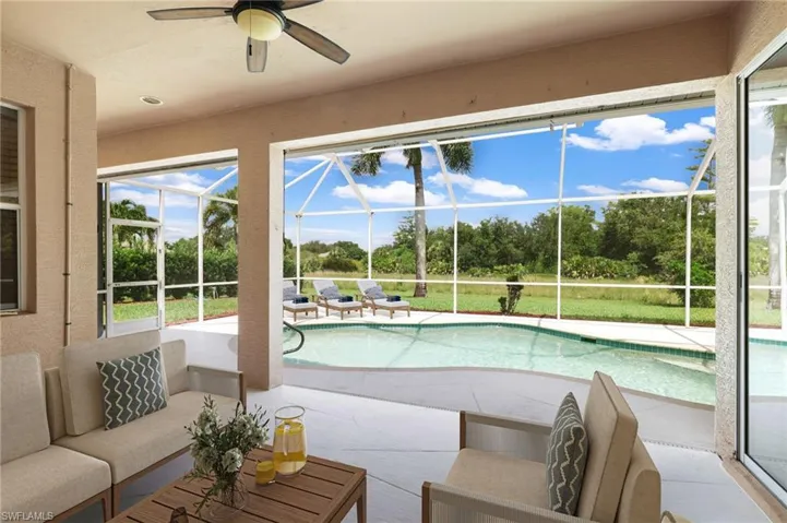 Swimming pool with a lanai, pool deck, a ceiling fan, and view of wooded area
