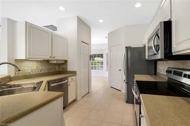 Kitchen featuring decorative backsplash, stainless steel appliances, light tile patterned flooring, recessed lighting, and white cabinetry