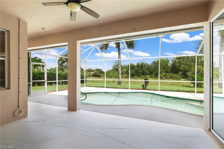 Swimming pool with a lanai, a patio, ceiling fan, and view of scattered trees