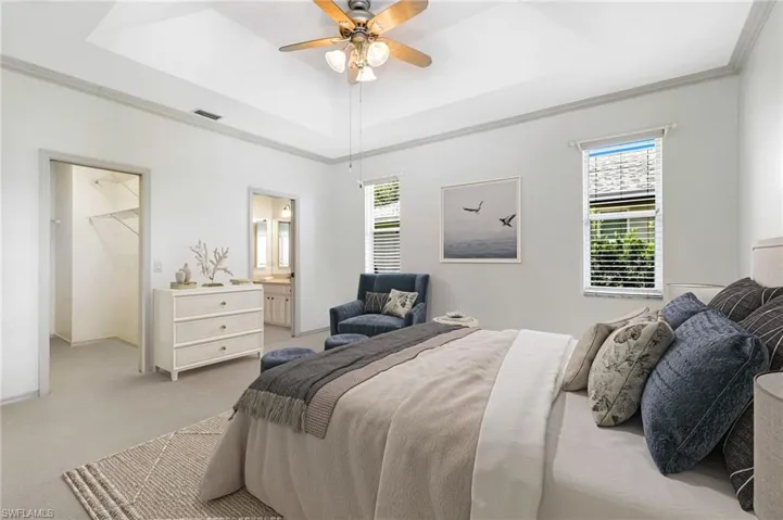 Primary Bedroom featuring ornamental molding, light carpet, a walk in closet, a raised ceiling, and a ceiling fan