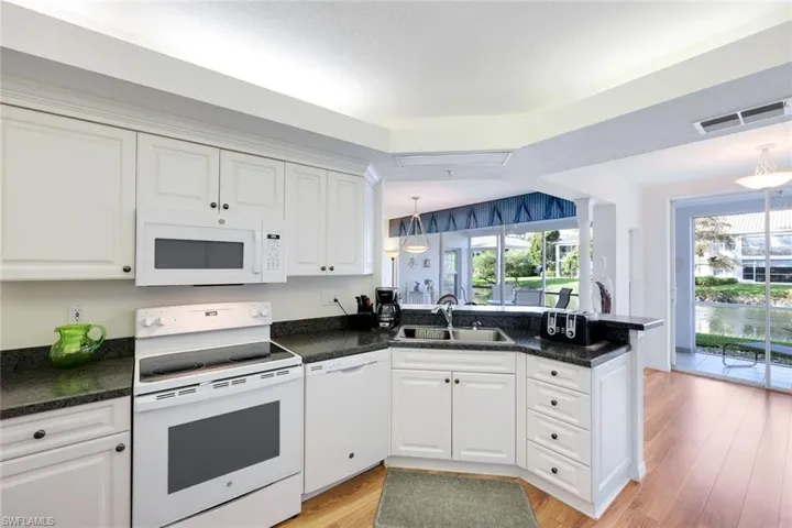 Kitchen featuring white appliances, sink, hanging light fixtures, light wood-type flooring, and white cabinetry