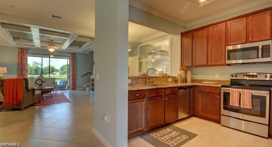 Kitchen featuring stainless steel appliances, light tile patterned flooring, light stone counters, wood finish cabinetry, and a ceiling fan