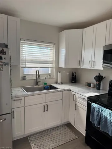 Kitchen featuring stove, white cabinetry, refrigerator, and dark wood-style floors