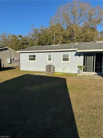 Back of house featuring concrete block siding, a lawn, a shingled roof, and a sunroom