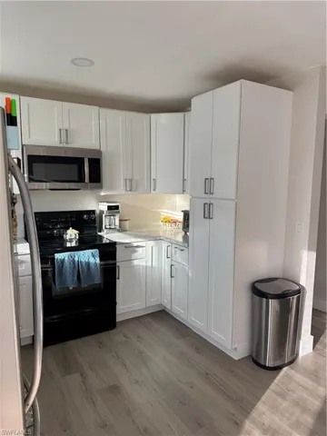 Kitchen with white cabinetry, stainless steel range oven, light wood-style flooring, and refrigerator