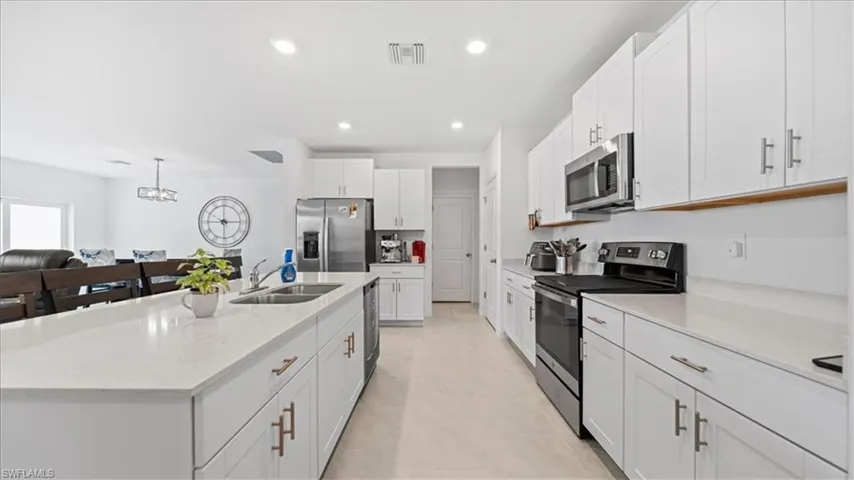 Kitchen featuring stainless steel appliances, white cabinetry, light stone counters, and a kitchen island with sink