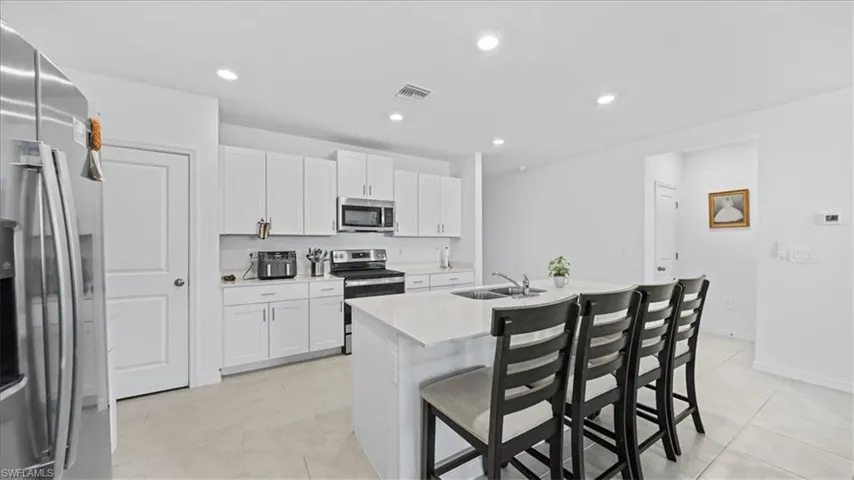 Kitchen with a kitchen bar, stainless steel appliances, white cabinetry, a kitchen island with sink, and recessed lighting