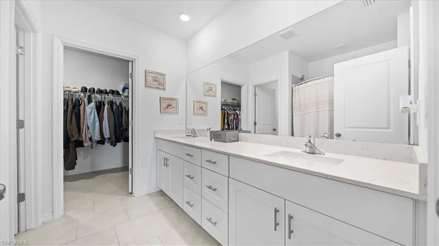 Full bath with a shower with curtain, double vanity, light tile patterned floors, and a spacious closet