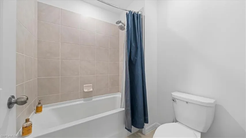 Bathroom featuring toilet and shower / bath combination with curtain