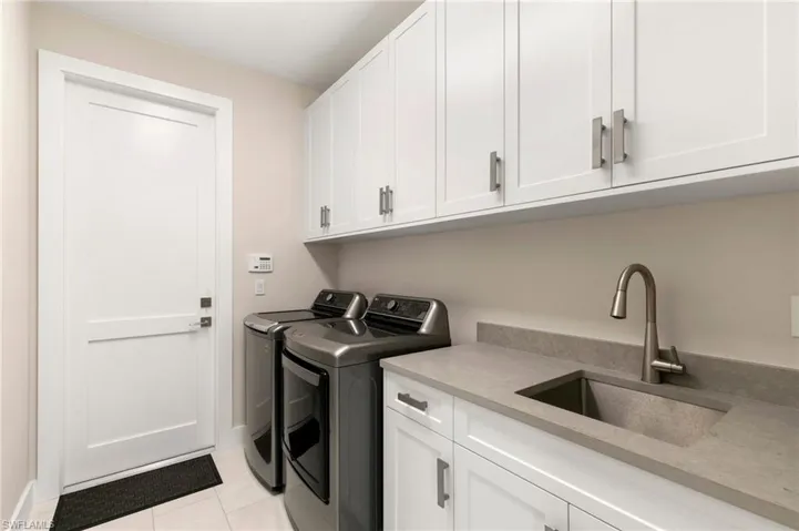 Washroom with sink, washing machine and clothes dryer, light tile patterned floors, and cabinets