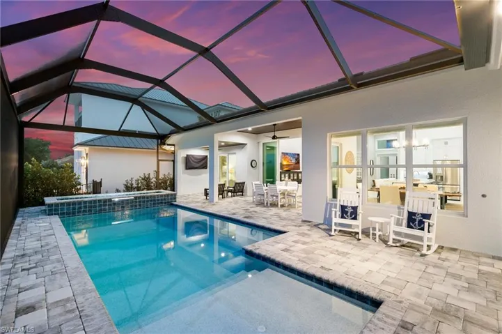 Pool at dusk with ceiling fan, screen enclosure, and a patio area