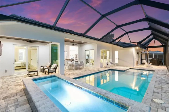 Pool at dusk with screen enclosure, a jacuzzi, ceiling fan, and a patio