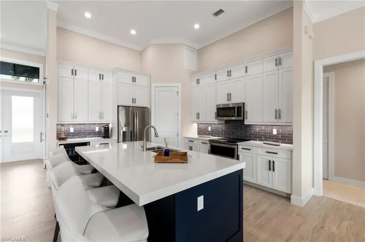Kitchen with light stone countertops, white cabinets, stainless steel appliances, an island with sink, and backsplash