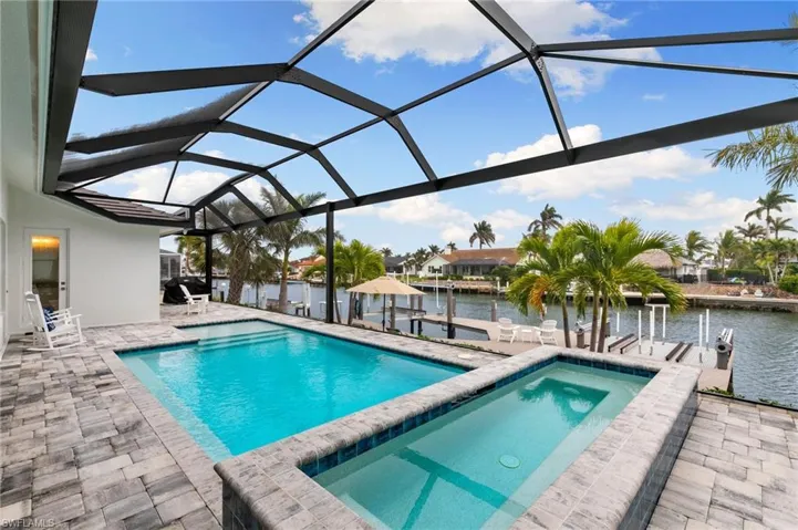 View of pool featuring screen enclosure, a boat dock, a water view, and a patio area