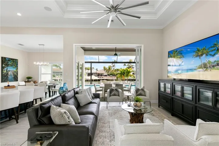 Living room featuring ceiling fan with notable chandelier, crown molding, and a tray ceiling