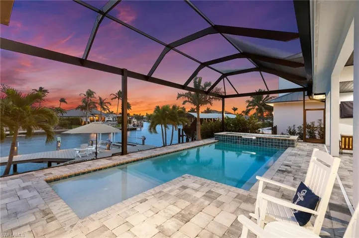 Pool at dusk with screen enclosure, an in ground hot tub, a boat dock, and a water view