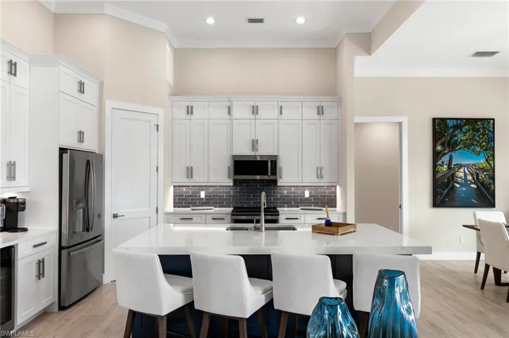 Kitchen with appliances with stainless steel finishes, sink, backsplash, white cabinetry, and a kitchen island with sink