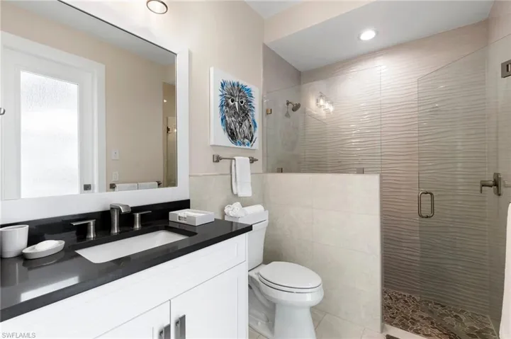 Bathroom featuring tile patterned floors, tile walls, toilet, a shower with shower door, and vanity