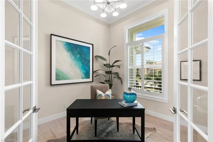Home office featuring light wood-type flooring, french doors, crown molding, and an inviting chandelier