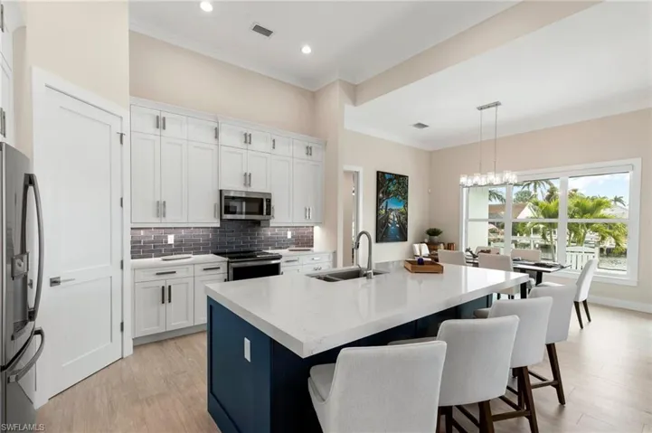 Kitchen with a kitchen island with sink, sink, white cabinets, decorative light fixtures, and stainless steel appliances
