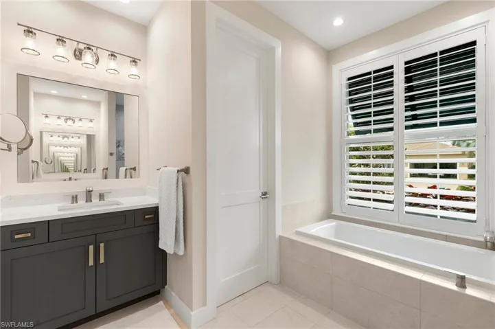 Bathroom with tile patterned flooring, tiled tub, and vanity