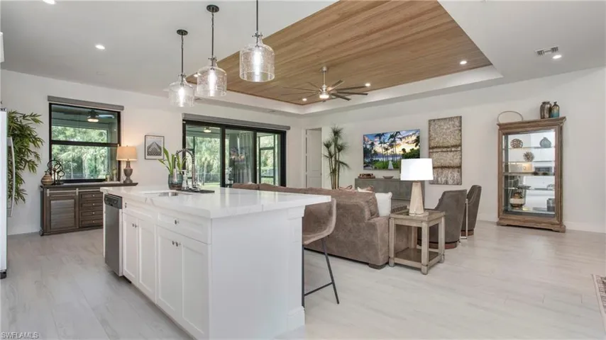 Kitchen featuring ceiling fan, a raised ceiling, a kitchen bar, white cabinetry, and light countertops