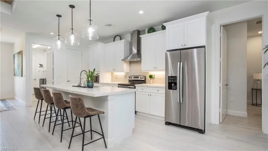 Kitchen featuring appliances with stainless steel finishes, wall chimney exhaust hood, an island with sink, recessed lighting, and backsplash