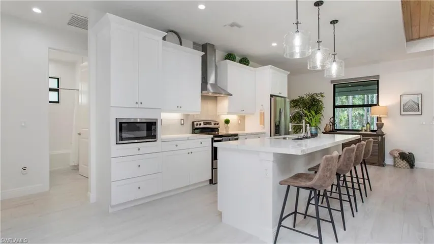 Kitchen featuring wall chimney exhaust hood, stainless steel appliances, a kitchen island with sink, backsplash, and recessed lighting