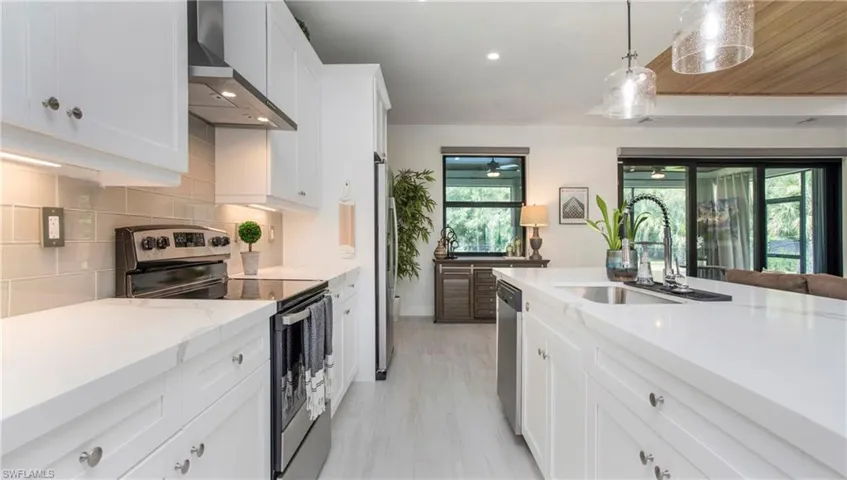 Kitchen featuring wall chimney range hood, appliances with stainless steel finishes, white cabinets, backsplash, and pendant lighting