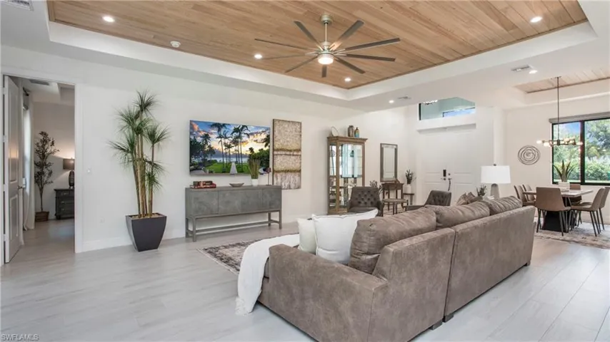 Living area featuring a tray ceiling, wood ceiling, a ceiling fan, light wood finished floors, and a chandelier