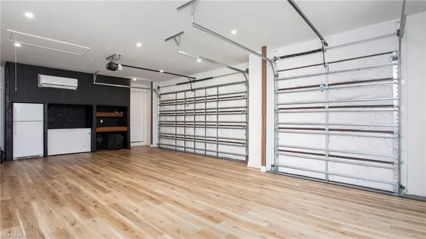 Garage with a garage door opener, a wall unit AC, and freestanding refrigerator