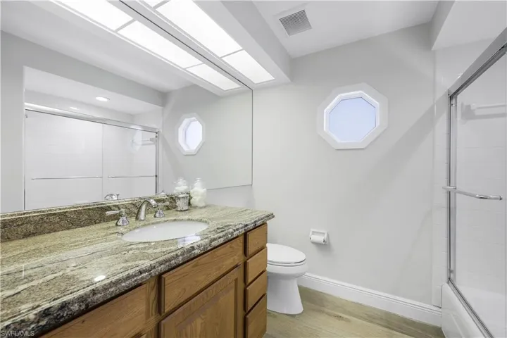 Bathroom featuring light wood-type flooring, plenty of natural light, vanity, and shower / bath combination with glass door