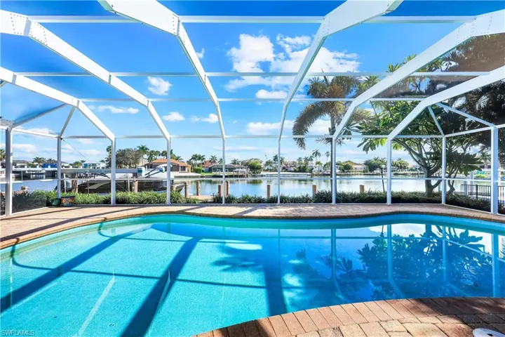 Swimming pool with a water view, glass enclosure, a sunroom, a residential view, and a patio