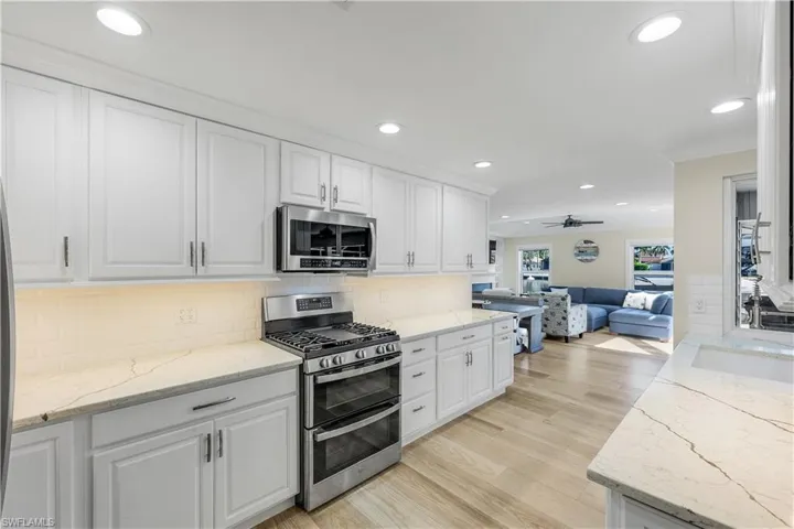 Kitchen with appliances with stainless steel finishes, light stone countertops, recessed lighting, white cabinetry, and open floor plan