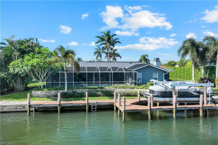 Back of house featuring glass enclosure, a sunroom, a water view, and boat lift