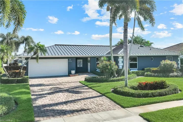 Ranch-style home with stucco siding, decorative driveway, a front yard, an attached garage, and a metal roof