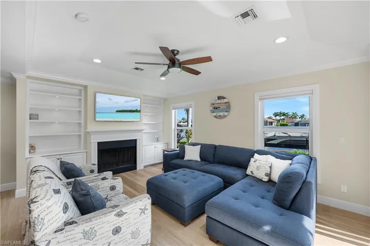 Living area featuring light wood-style floors, a sunroom, crown molding, a fireplace, and ceiling fan