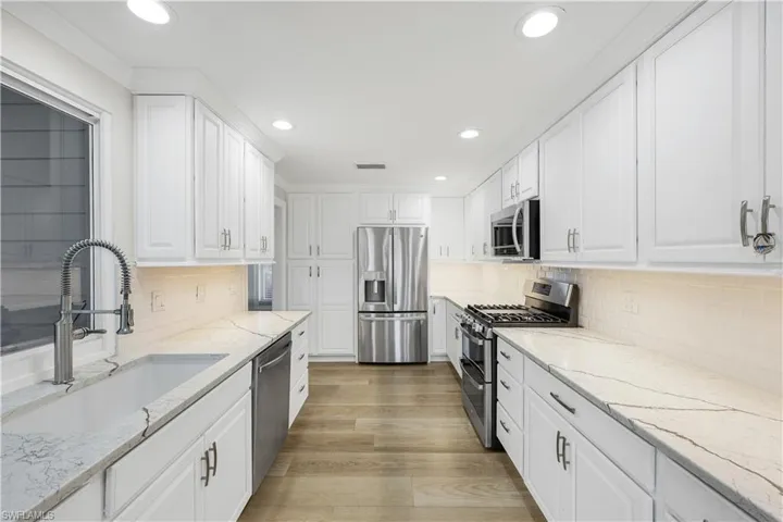 Kitchen with light stone countertops, appliances with stainless steel finishes, white cabinets, light wood-style floors, and recessed lighting