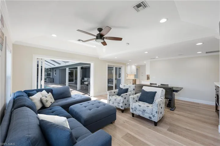 Living room with crown molding, light wood-style flooring, a ceiling fan, built in features, and a fireplace