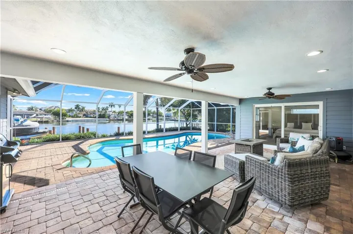 View of patio featuring a water view, a sunroom, ceiling fan, an outdoor pool, and glass enclosure