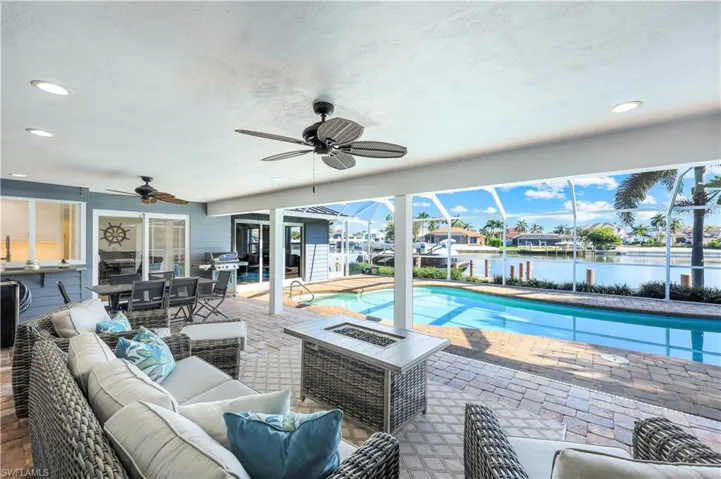 Outdoor pool featuring outdoor dining space, an outdoor living space with a fire pit, a water view, a patio, and area for grilling