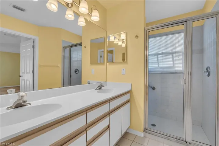 Bathroom with tile patterned floors, dual vanity, and a shower with shower door